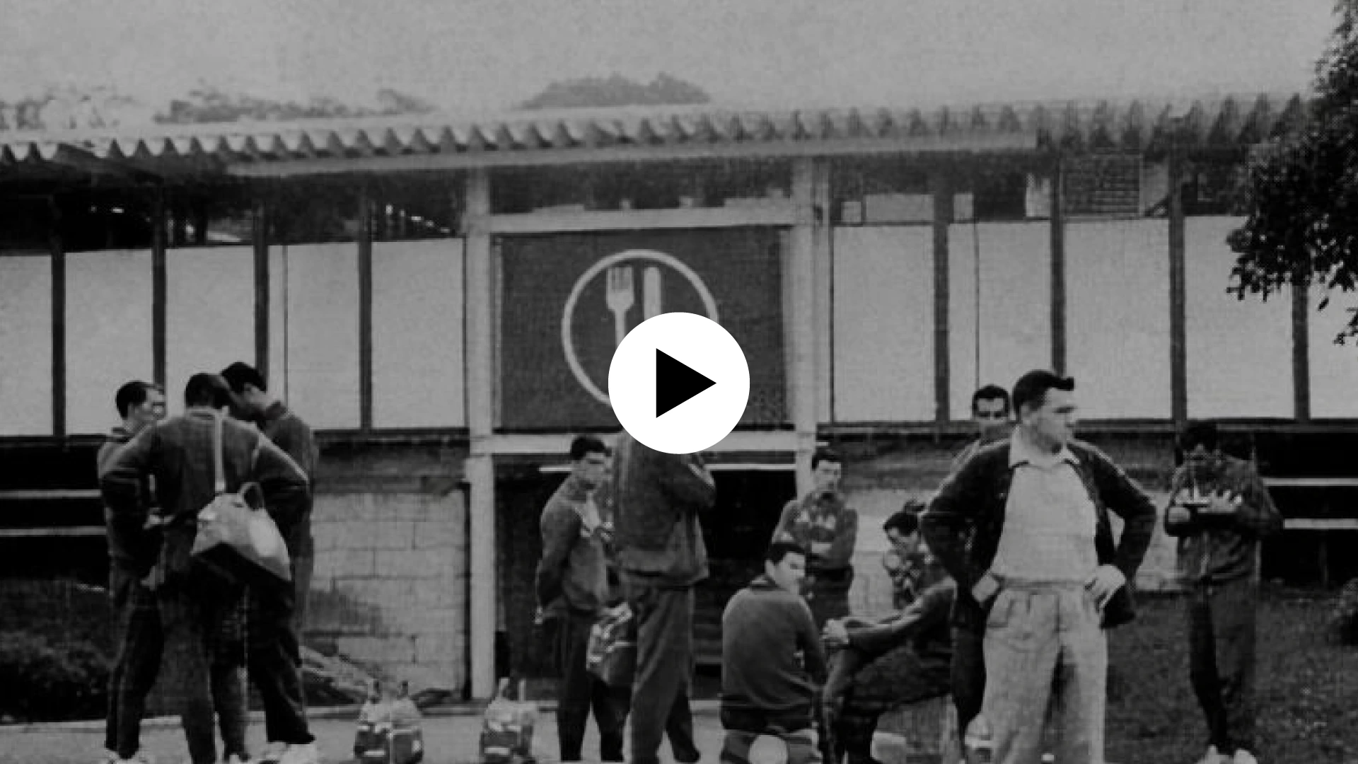 Image d'archive d'un bâtiment affichant un pictogramme issu de la charte graphique des jeux olympiques de Tokyo 1964. Icône play en surimpression indiquant que l'image est cliquable et mène vers un contenu vidéo.