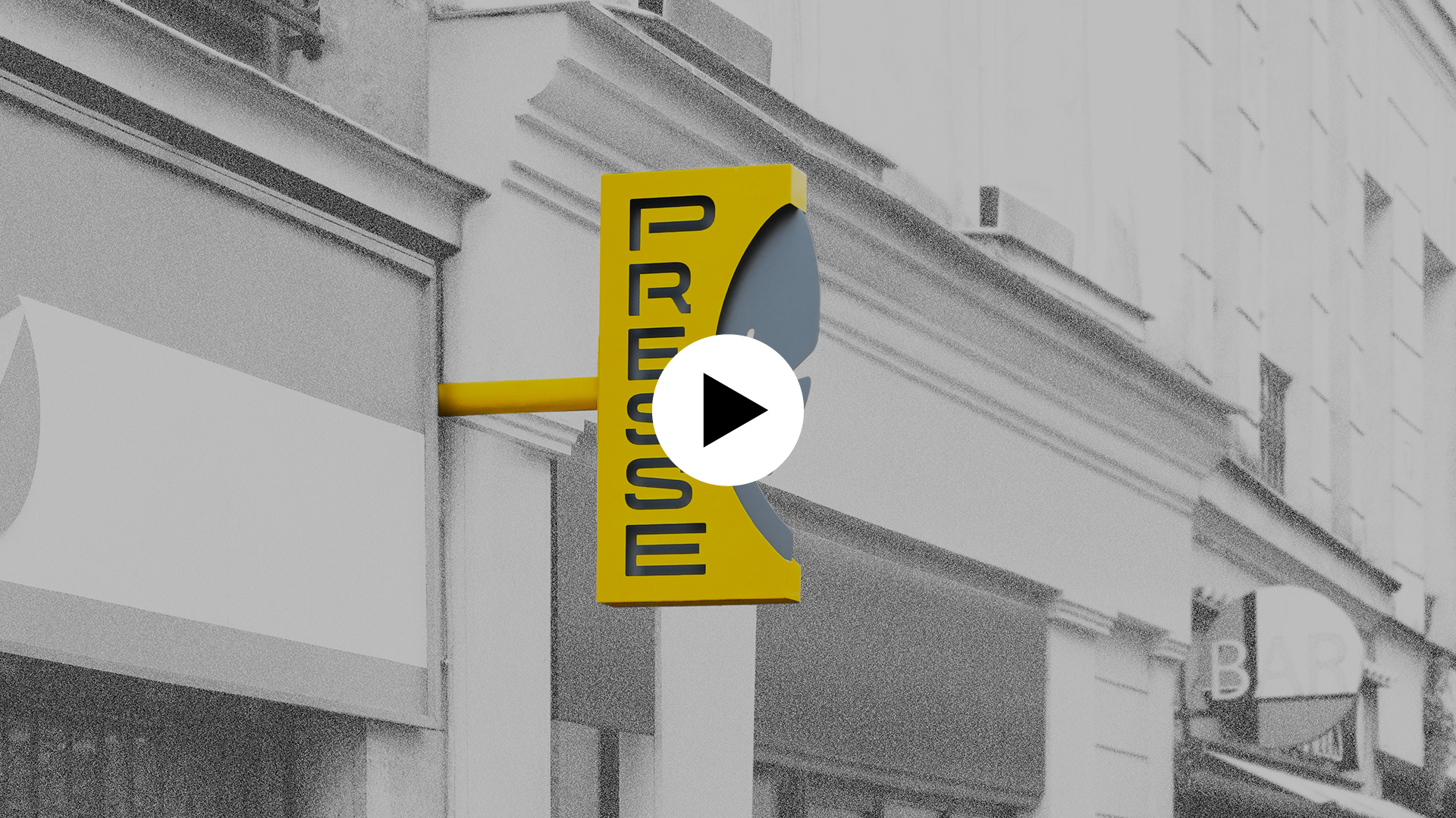 Image de la nouvelle enseigne posée sur une facade d'immeuble ; l'enseigne est en couleur, le reste de l'image en noir et blanc. Icône play en surimpression indiquant que l'image est cliquable et mène vers un contenu vidéo.